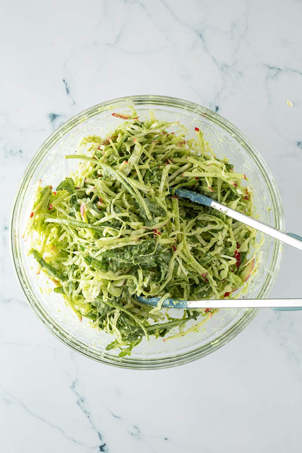 Wei&szlig;kohlsalat mit d&uuml;nnen Apfelstiften, Rucola und gr&uuml;ner Sauce in einer Glassch&uuml;ssel vermischt.