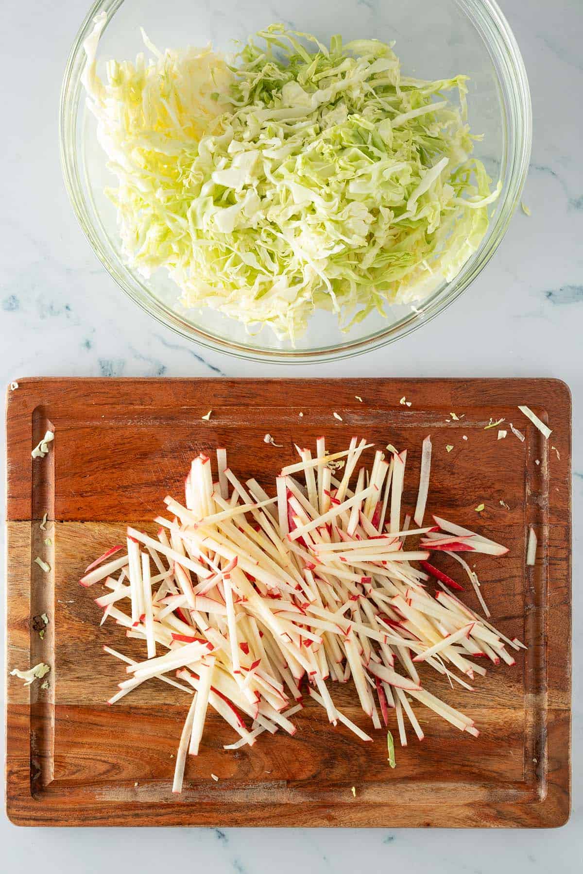 Fein geschnittener Wei&szlig;kohl in einer Glassch&uuml;ssel und feine Apfelstifte auf einem Holzbrett.