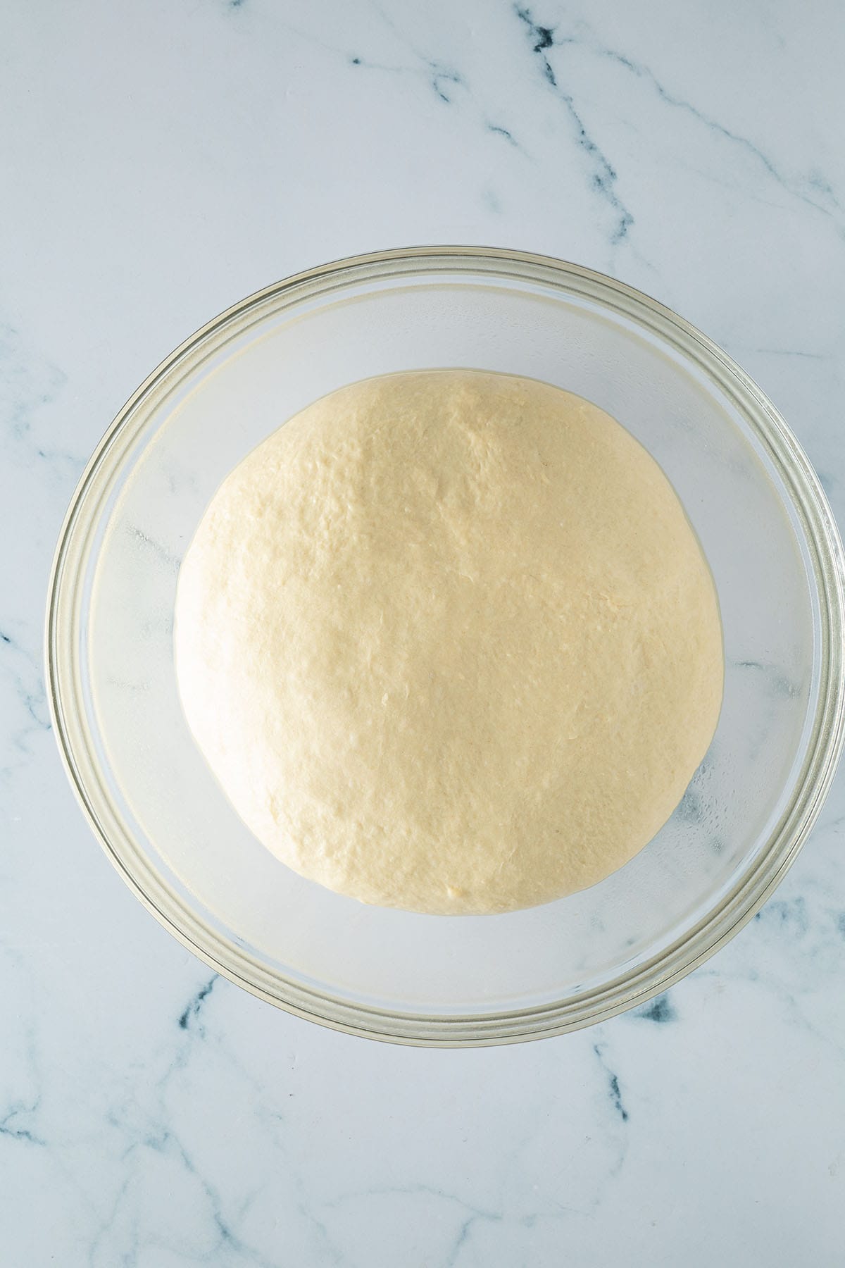 Aufgegangener Hefeteig f&uuml;r H&uuml;ttenk&auml;se Brot in einer gro&szlig;en Glassch&uuml;ssel.