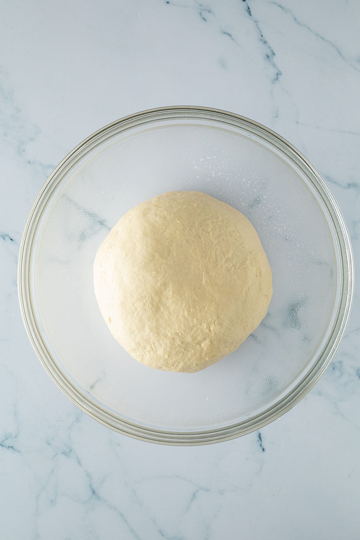 Zu einer Kugel geformter Hefeteig in einer gro&szlig;en Glassch&uuml;ssel.