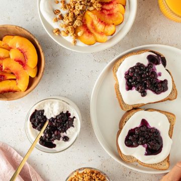 Verschiedene Frühstücks-Gerichte mit der süßen Hüttenkäse-Creme auf einem hellen Untergrund.