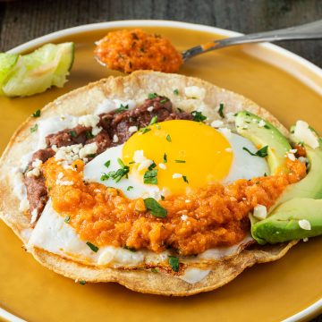 Knuspriger Tortilla mit Bohnenmus, Spiegelei und Salsa auf einem Teller.