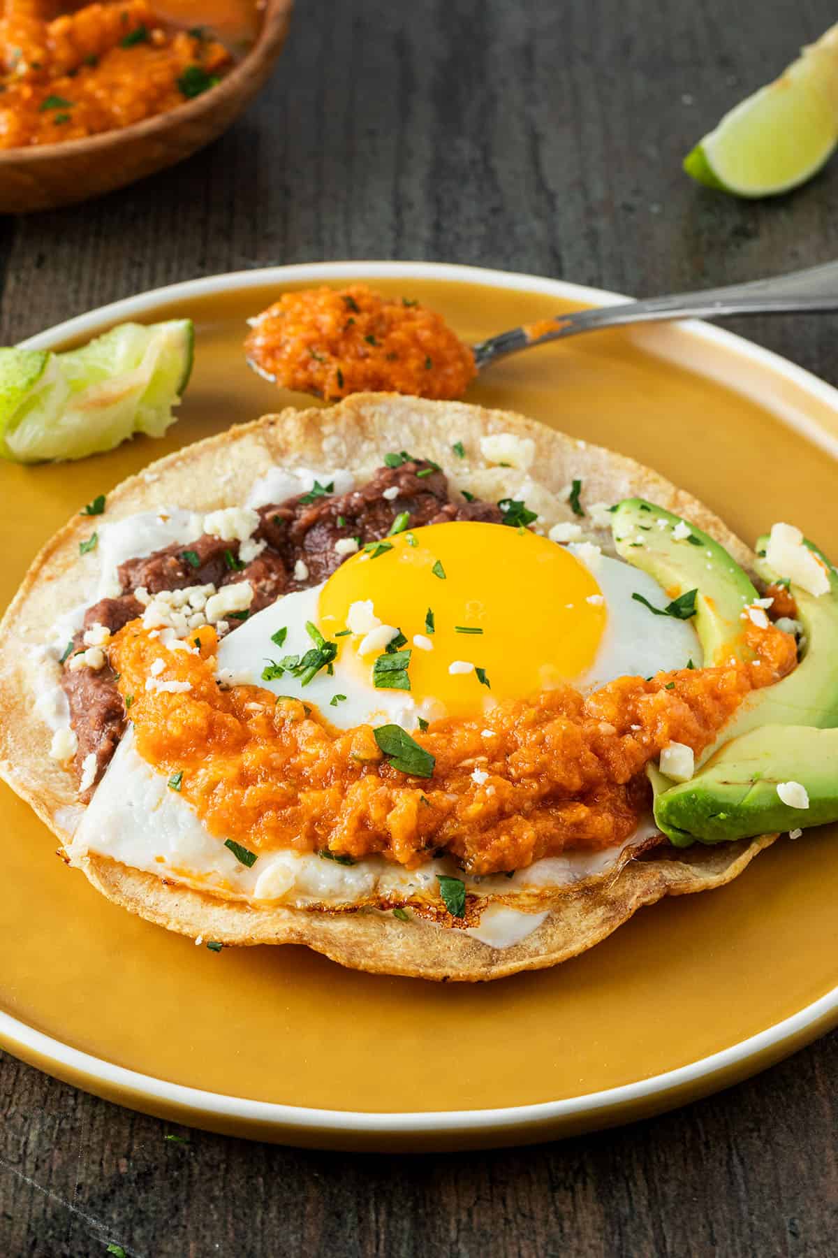 Knuspriger Tortilla mit Bohnenmus, Spiegelei und Salsa auf einem Teller.