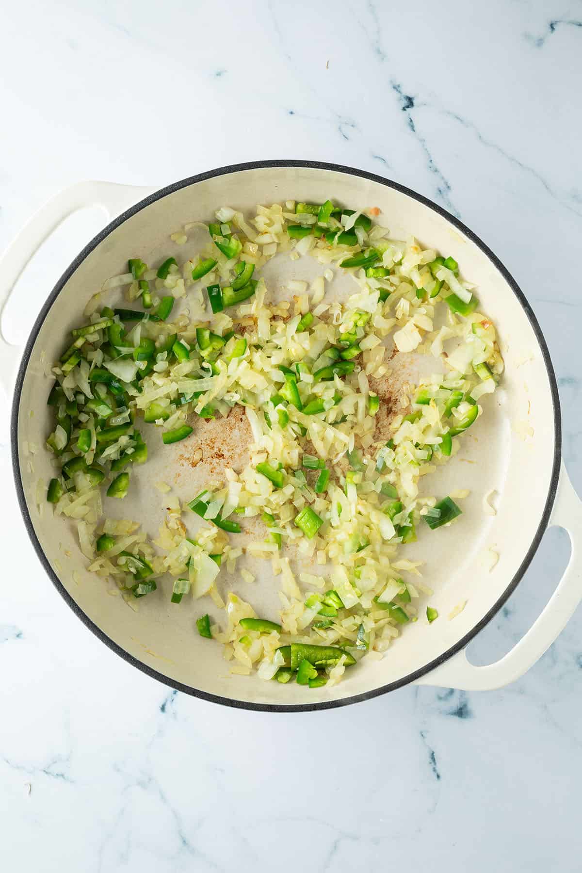 Zwiebeln, Knoblauch und Jalapeño werden in einer großen Pfanne angebraten.
