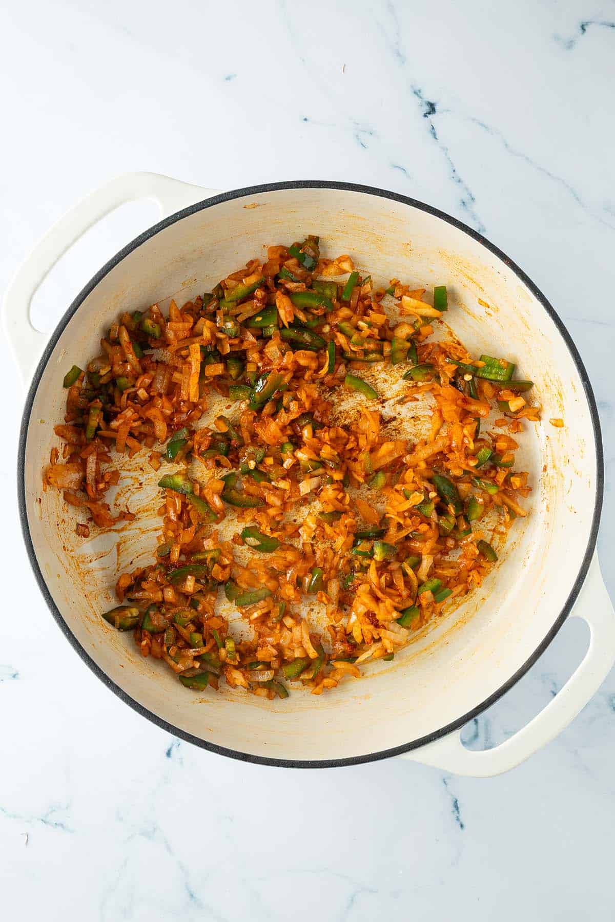 Zwiebeln, Knoblauch und Jalapeño werden mit den Gewürzen in der Pfanne angebraten.