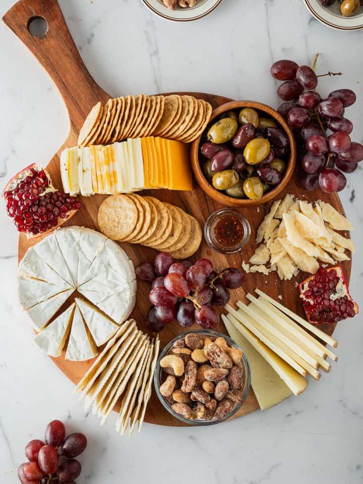 Käseplatte mit verschiedenen Käsesorten, Crackern, Trauben, Oliven, Nüssen und Granatapfel von oben fotografiert.