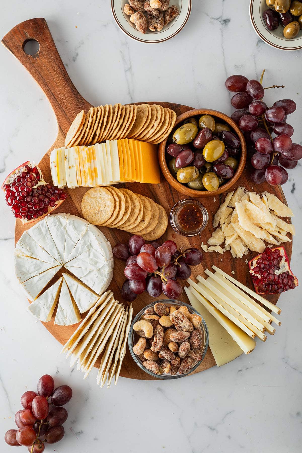 K&auml;seplatte mit verschiedenen K&auml;sesorten, Crackern, Trauben, Oliven, N&uuml;ssen und Granatapfel von oben fotografiert.