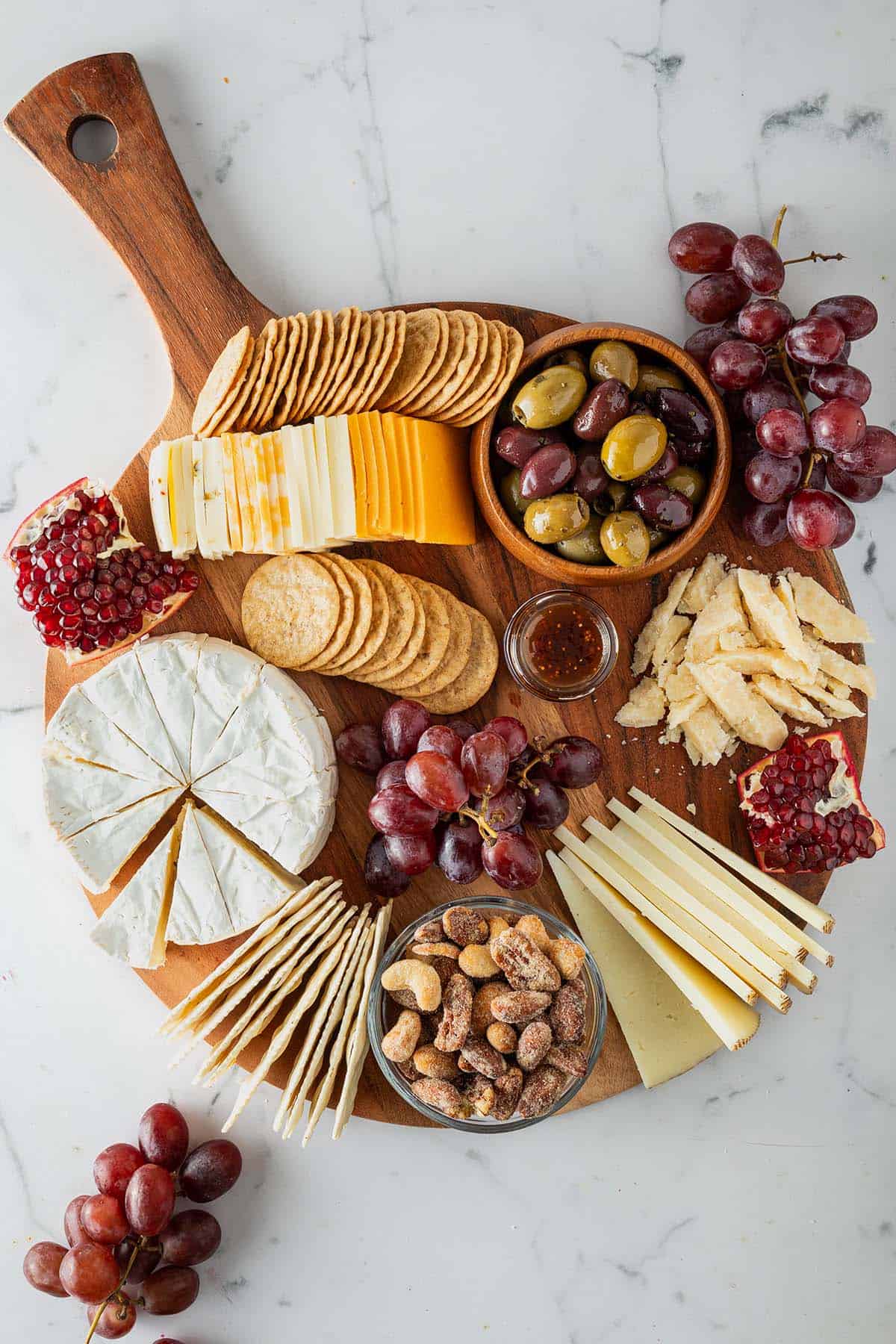 Fertig angerichtete Käseplatte mit Weichkäse, Schnittkäse, Oliven, Crackern, Trauben und Parmesan-Spänen.