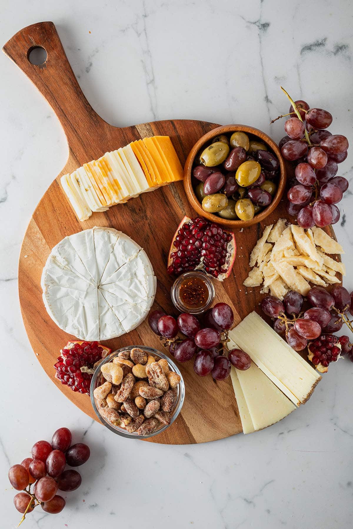 Teilweise angerichtete Käseplatte mit verschiedenen, angeschnittenen Käsesorten, Nüsse, Oliven und Obst.