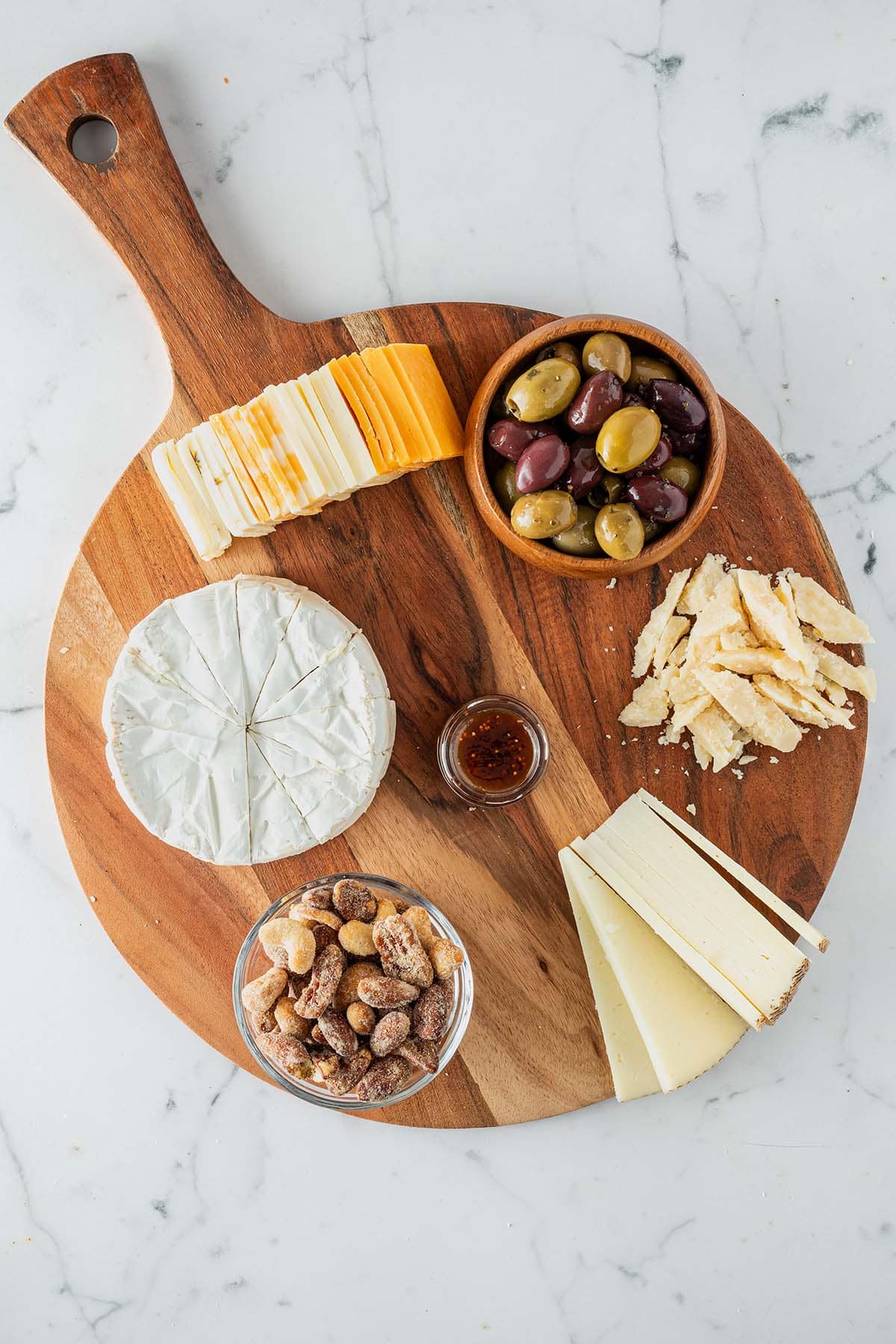 Angeschnittener Käse drapiert auf einem Holzbrett mit einer Schüssel Oliven, Nüsse und einer Feigenmarmelade.