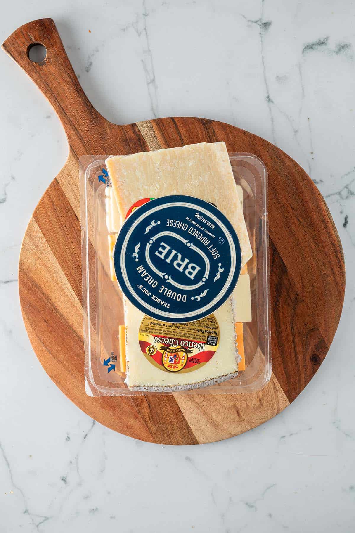 Verpackte Käsesorten auf einem Holzbrett als Ausgangspunkt für eine Käseplatte.