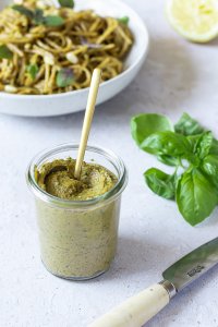 Kalorienarmes und gesundes Pesto mit Basilikum in einem kleinen Weck-Gläschen, im Hintergrund ein Teller Nudeln.