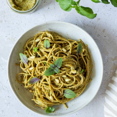 Ein Teller Spaghetti mit gesunder, kalorienarmer Pesto, daneben ein Topf Basilikum und ein Glas mit dem selbstgemachten, gesunden Pesto.
