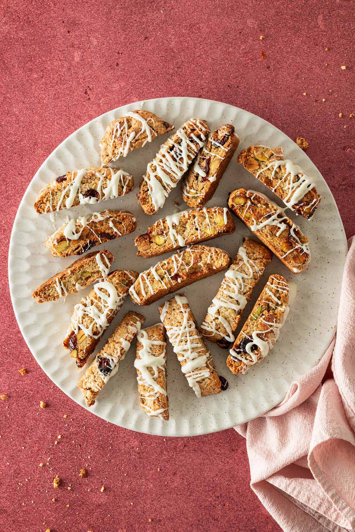Kardamom-Cantuccini mit Cranberries und Pistazien auf einem Teller, mit weißer Schokolade dekoriert.