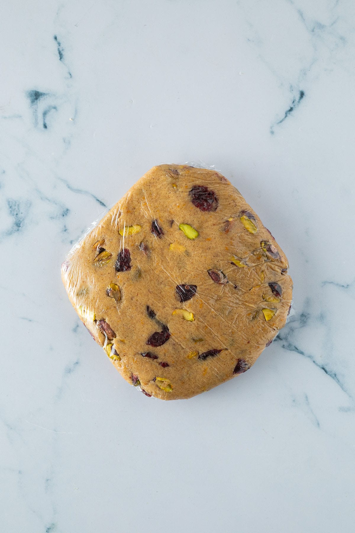 Fertiger Kardamom-Plätzchen-Teig mit Pistazien und Cranberries in Frischhaltefolie gewickelt.