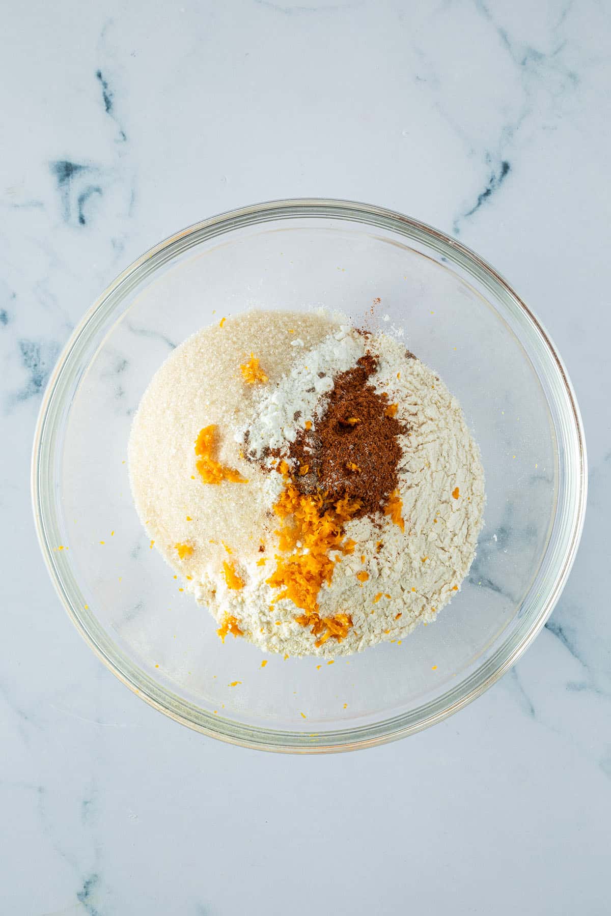Mehl, Zucker, Orangenschale und Gewürze in einer Glasschüssel.