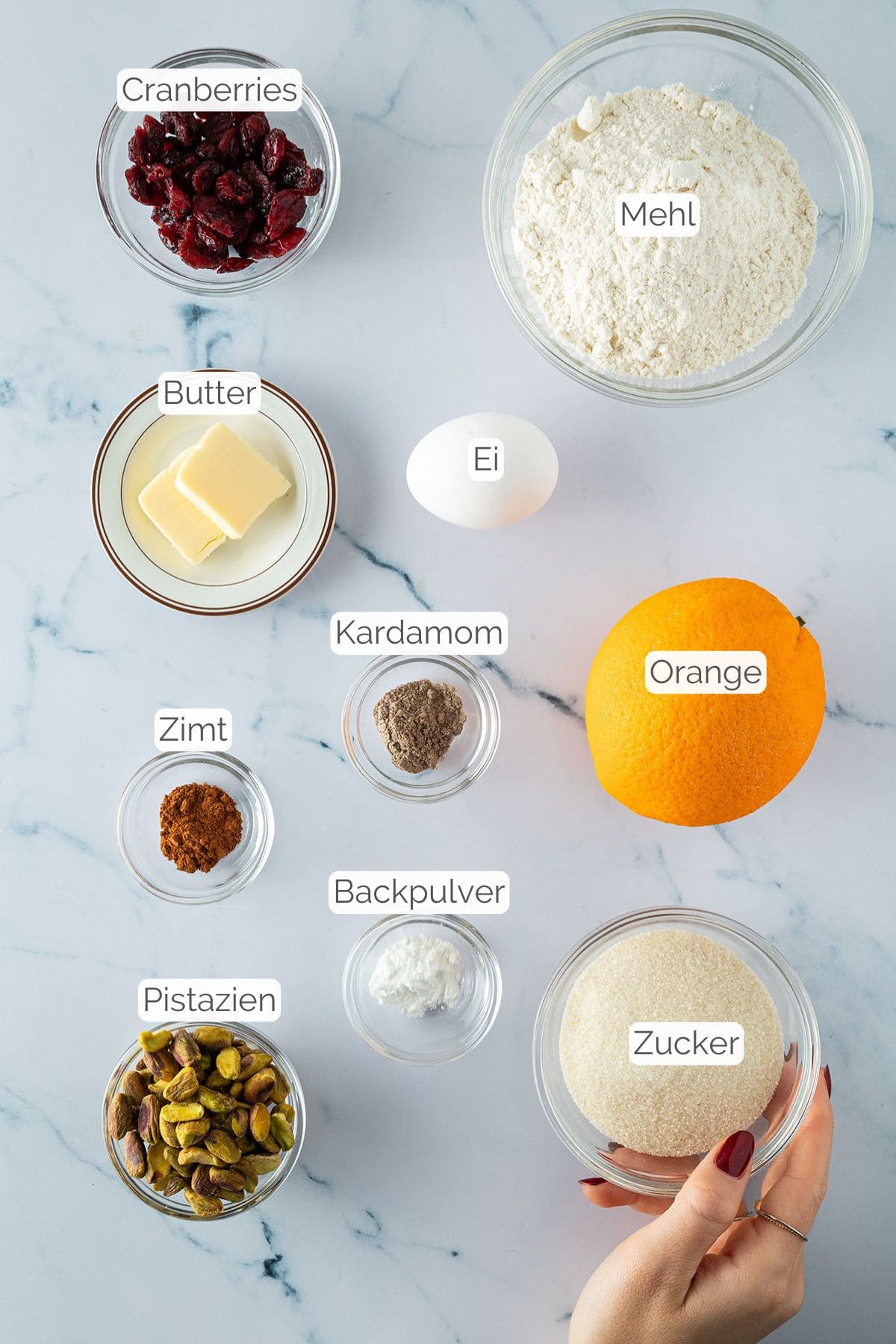 Zutaten für Kardamom-Plätzchen mit Pistazien und Cranberries, einzeln beschriftet und angeordnet.