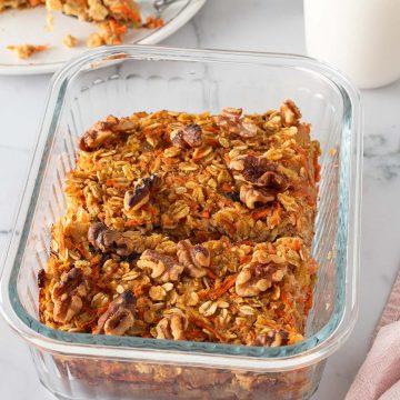 2 Portionen Karotten-Baked-Oats in einer Glasform, goldbraun gebacken mit Walnüssen, eine Portion auf einem Teller mit einem Glas mit Milch im Hintergrund.