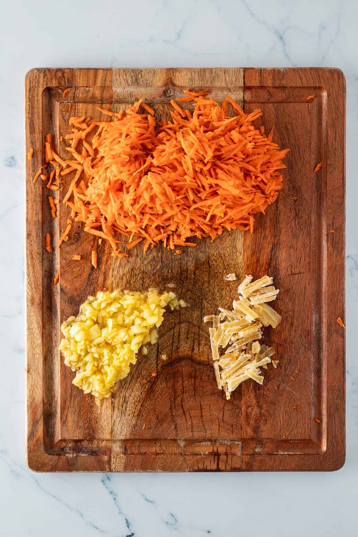 Geraspelte Karotten, fein gehackte Ananas und in dünne Streifen geschnittener, kandierter Ingwer auf einem Holzbrett.