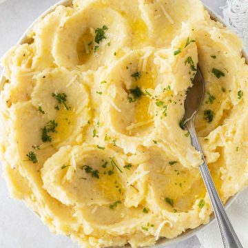 Ein luftiges Kartoffelpüree in einer Schüssel mit Petersilie, etwas geschmolzener Butter und geriebenen Käse als Garnitur.