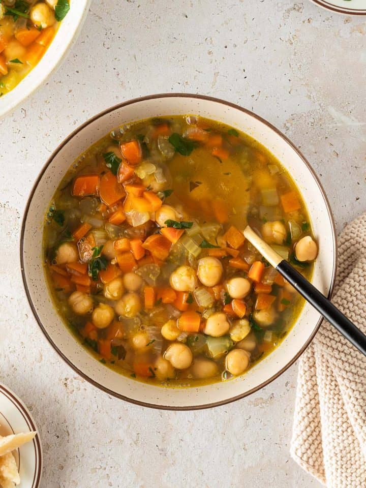 Schüssel mit Kichererbseneintopf aus Karotten, Sellerie und Brühe, Servierszene von oben fotografiert.