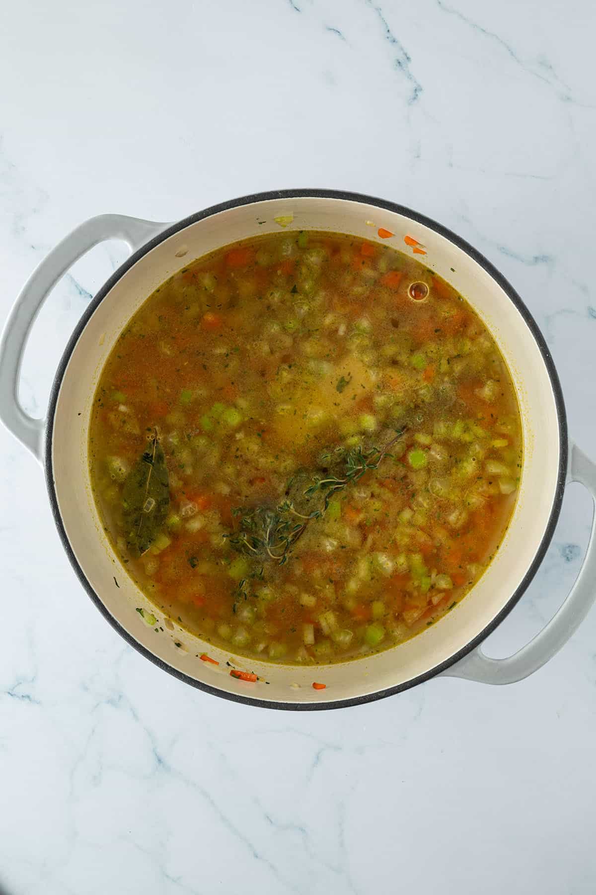 Großer Topf mit klarer Gemüsebrühe, feinem Suppengemüse und Kräutern und Kichererbsen.