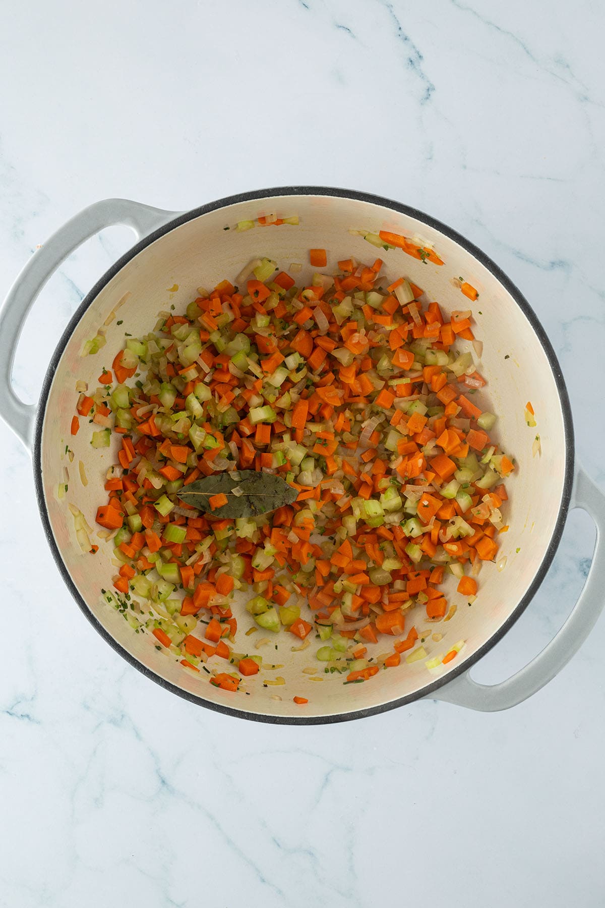 Angeschwitztes Suppengemüse aus Karotten, Sellerie und Zwiebeln im Topf.