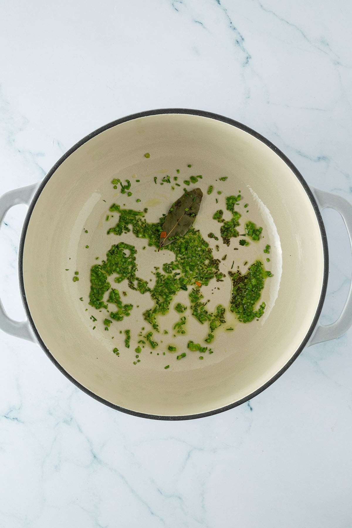 Ein Lorbeerblatt und fein gehackte Petersilienstängel werden in einem Topf mit Öl angebraten.