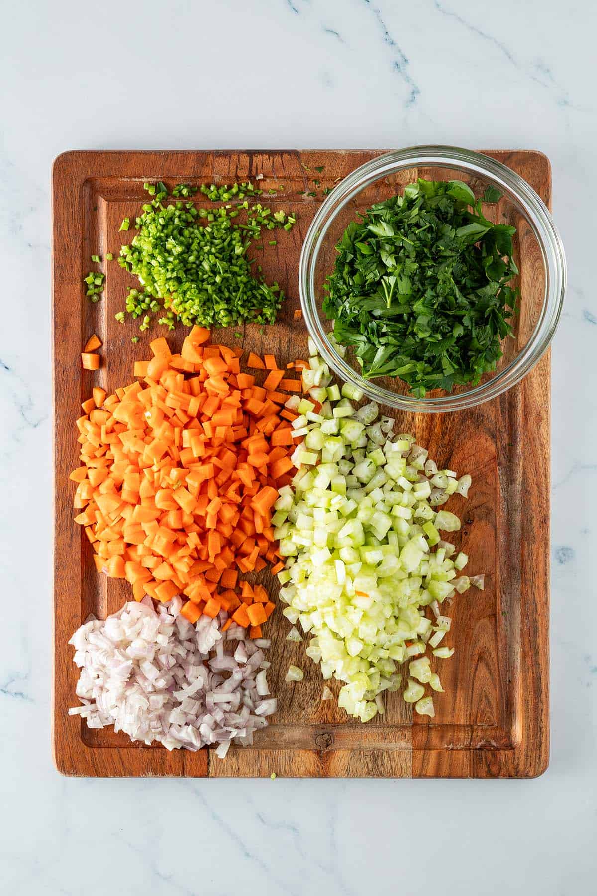 Fein gewürfelte Karotten, Sellerie, Schalotten und Petersilie auf einem Holzbrett.