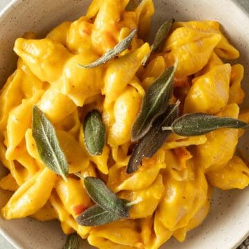 Cremiges Kürbis Mac and Cheese mit Muschelnudeln in einer Schüssel, garniert mit knusprigen Salbeiblättern.