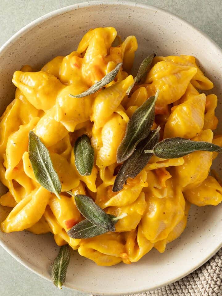 Cremiges Kürbis Mac and Cheese mit Muschelnudeln in einer Schüssel, garniert mit knusprigen Salbeiblättern.