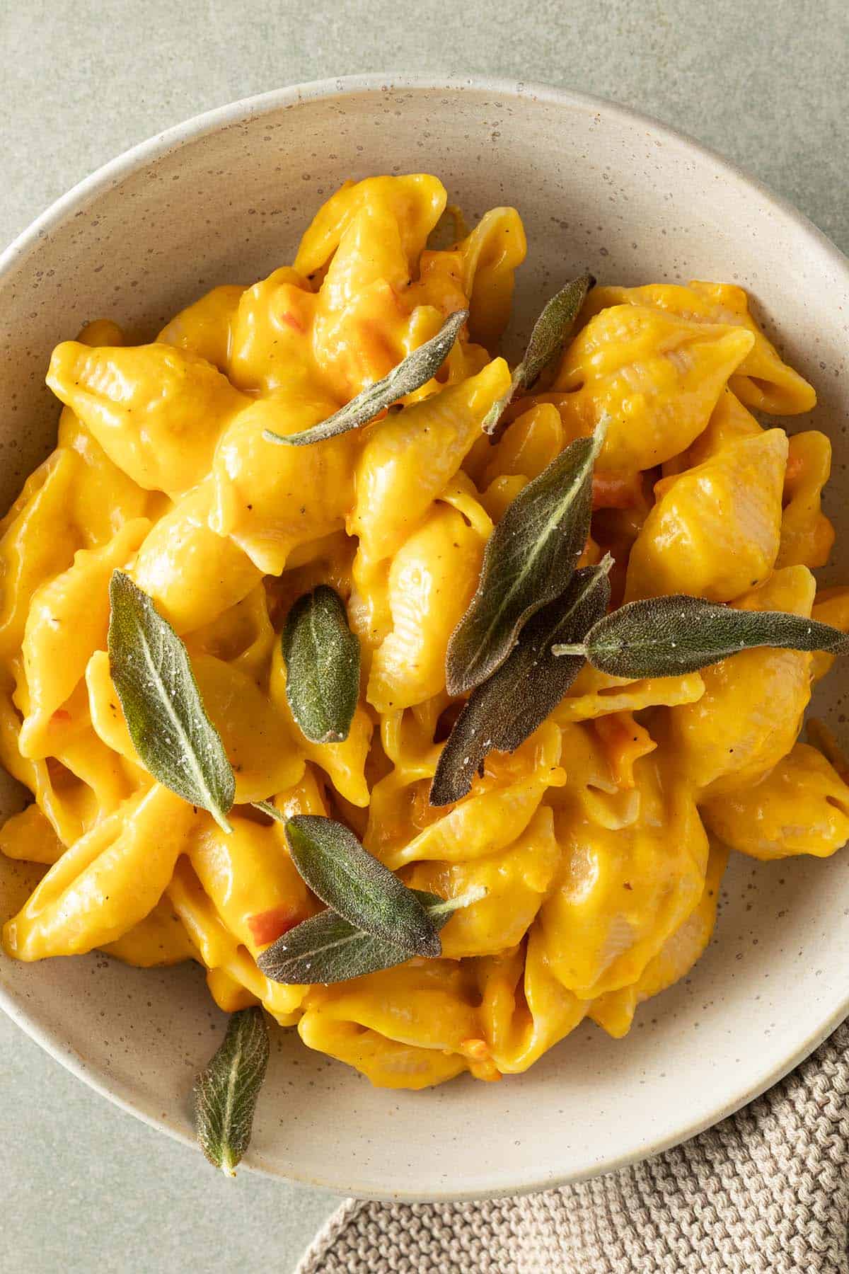Cremiges Kürbis Mac and Cheese mit Muschelnudeln in einer Schüssel, garniert mit knusprigen Salbeiblättern.