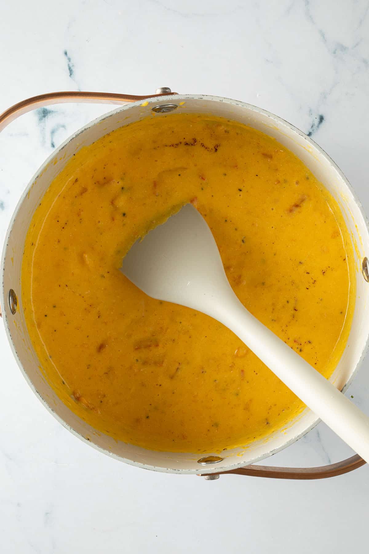 Cremige, orangefarbene Kürbis-Käsesauce in einem Topf, gewürzt mit Muskat.