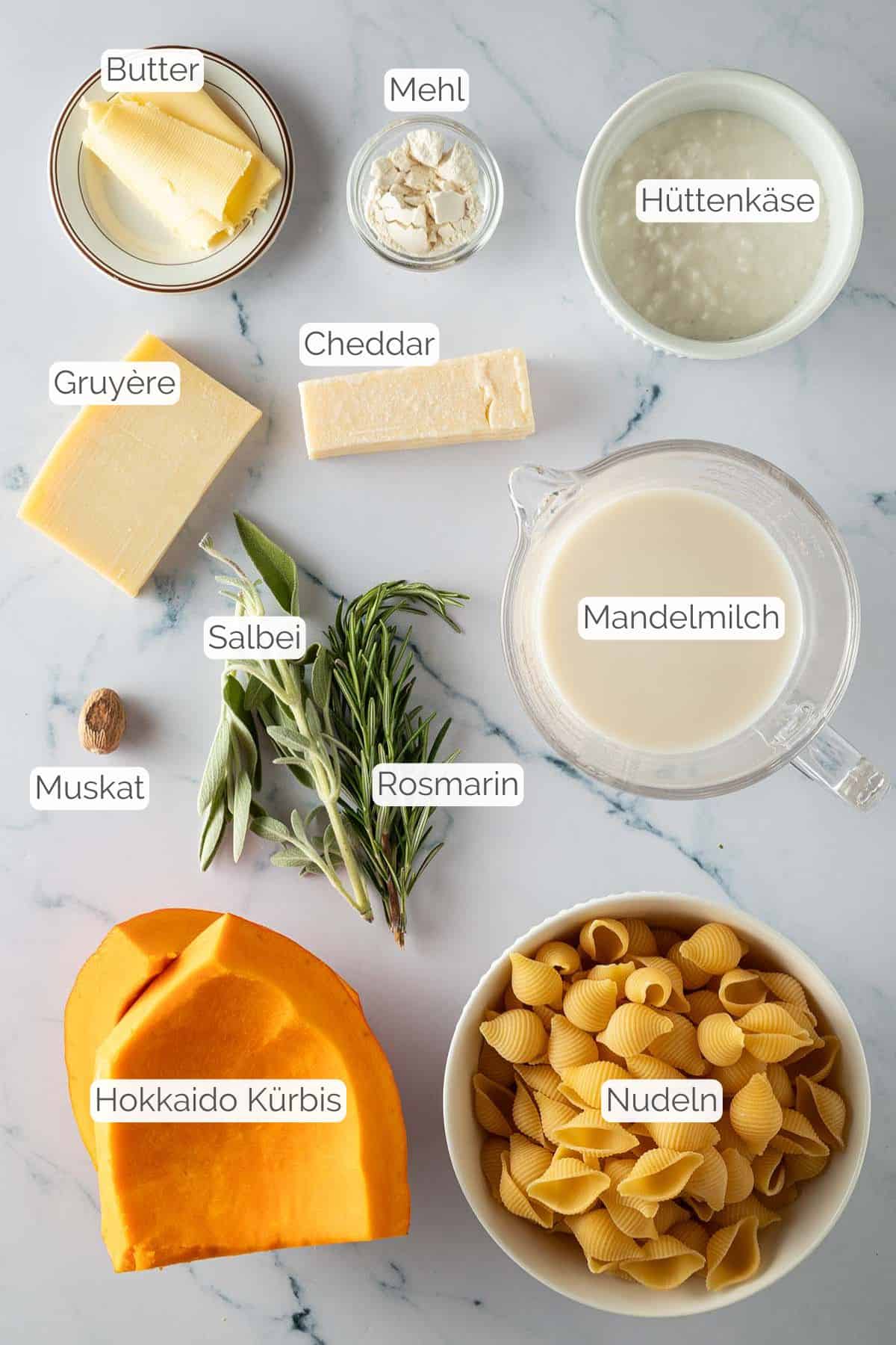 Alle Zutaten mit jeweiligen Textbeschriftungen, die für die Zubereitung von Kürbis Mac and Cheese benötigt werden.
