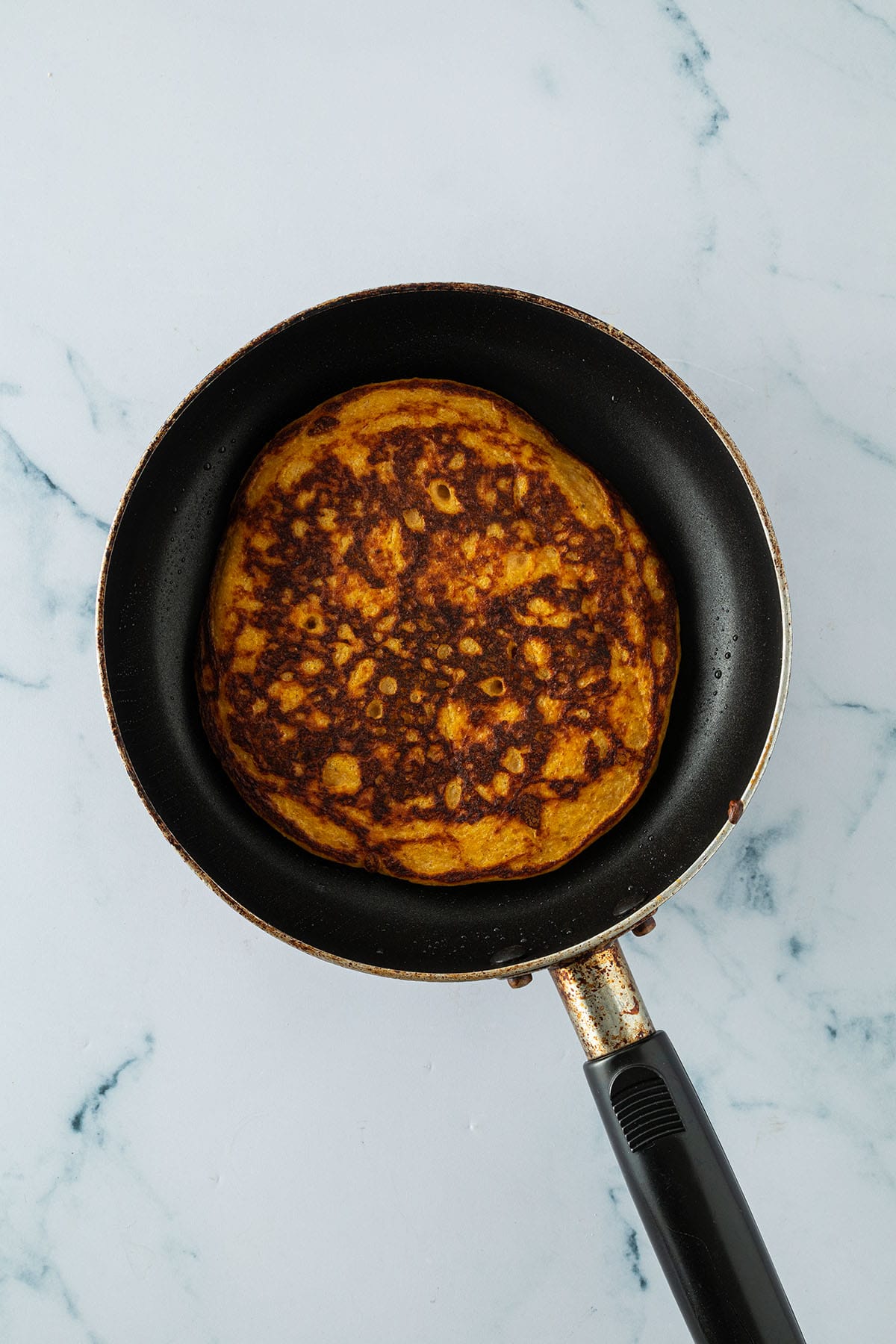 Angebratener, goldbrauner Kürbis Pancake in einer kleinen Pfanne.