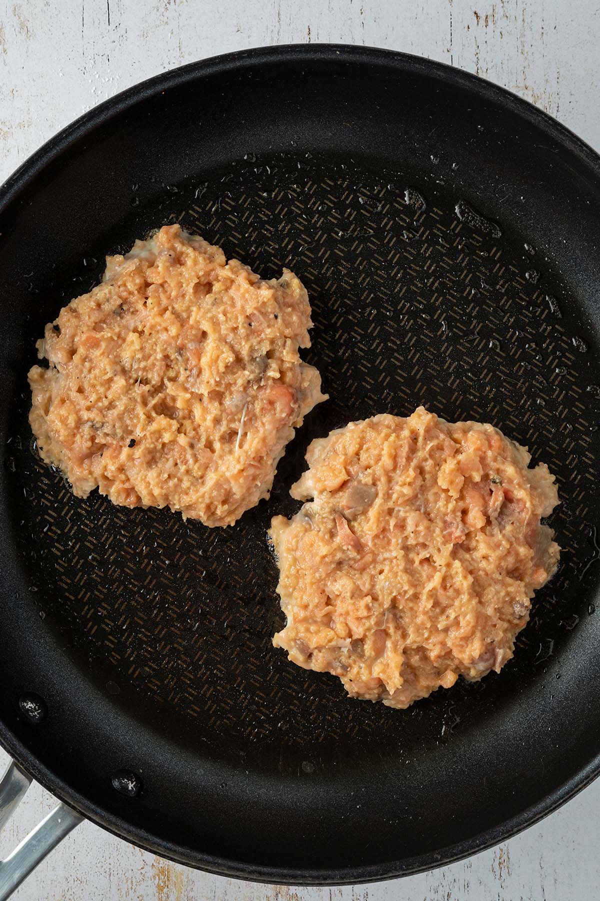 Aus der leicht Stückigen Lachsmasse wurden zwei Patties geformt, die in einer Pfanne angebraten werden.