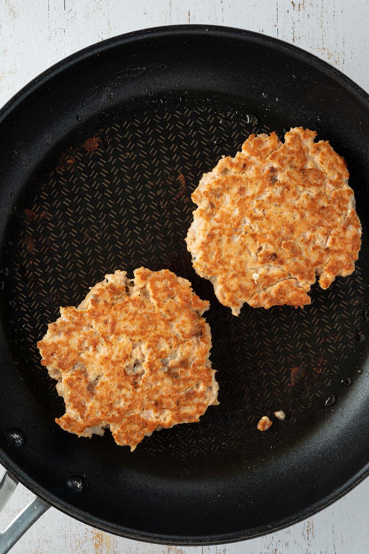 Goldbraun angebratene Lachs Patties in einer Pfanne.