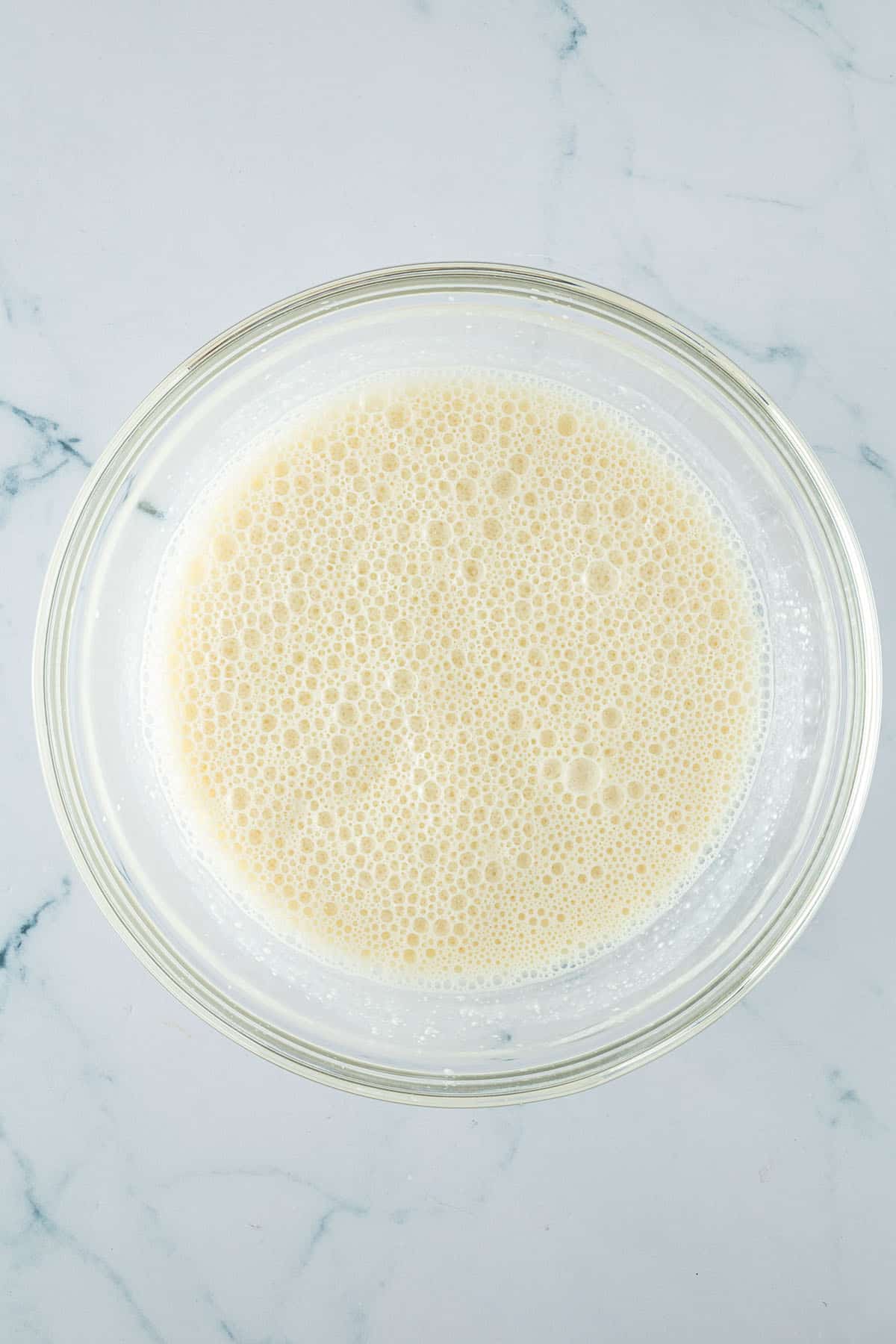 Glas-Rührschüssel mit einer hellen, schaumigen Flüssigmasse aus Eiern, Sojamilch und Hüttenkäse.