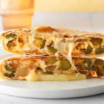 Halbiertes meal prep Frühstücksandwich aufeinandergestapelt, gefüllt mit geschmolzenem Käse und einem Omelett mit Paprika und Kartoffeln.