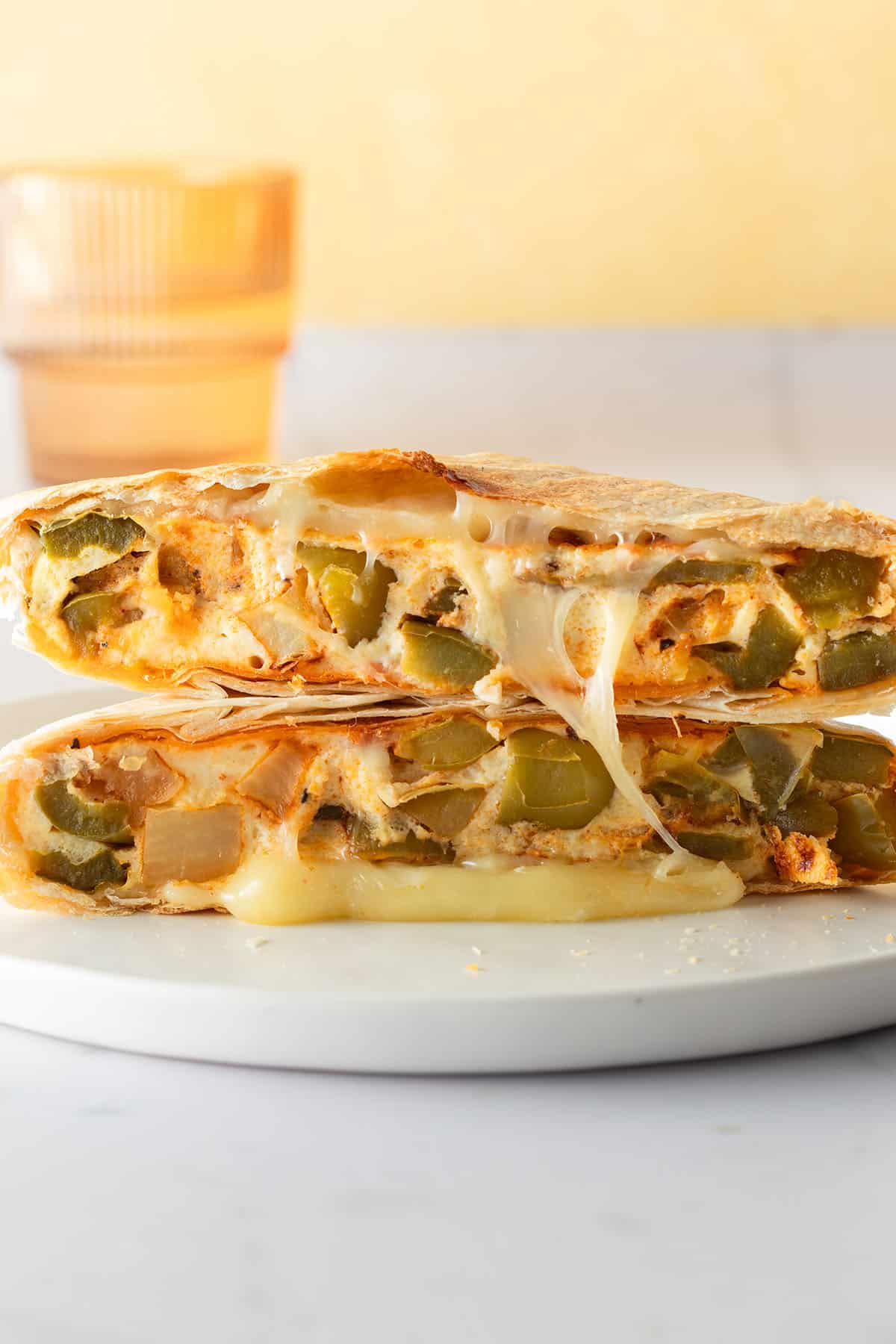 Halbiertes meal prep Frühstücksandwich aufeinandergestapelt, gefüllt mit geschmolzenem Käse und einem Omelett mit Paprika und Kartoffeln.