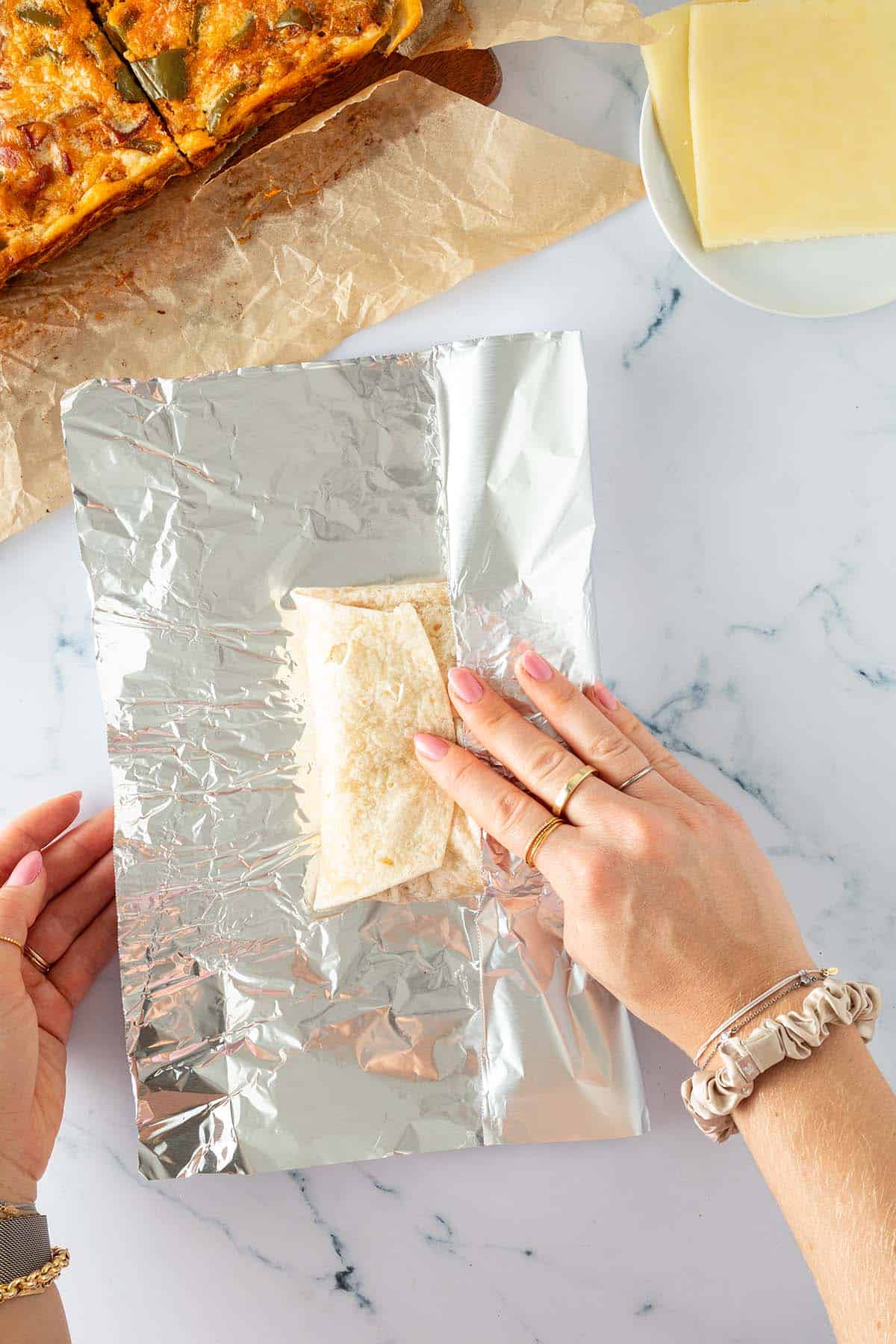 Hände wickeln ein gefülltes Frühstückssandwich aus Tortilla in Alufolie.