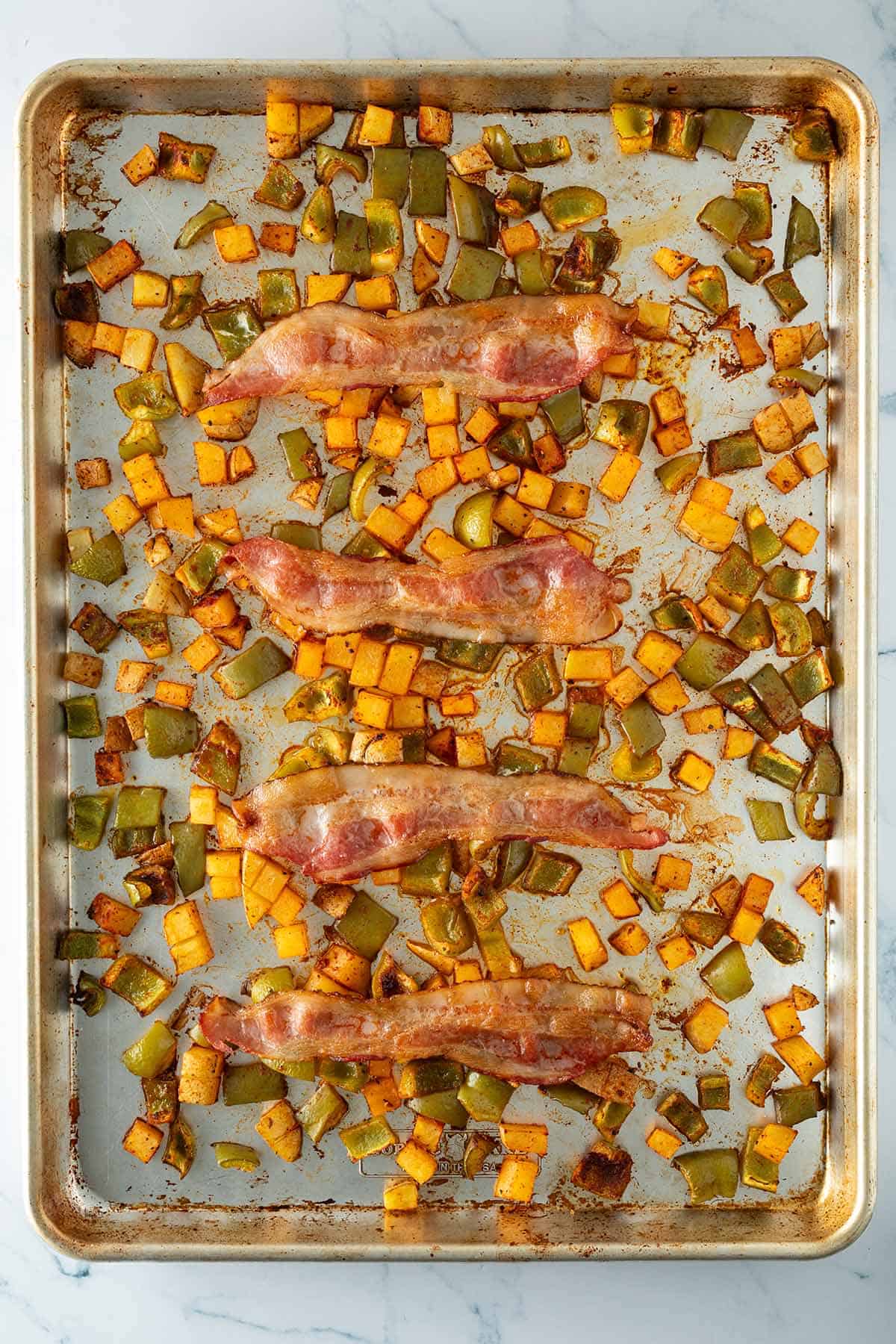 Geröstete Paprika, Kartoffeln und 4 knusprige Speckstreifen auf einem Blech.