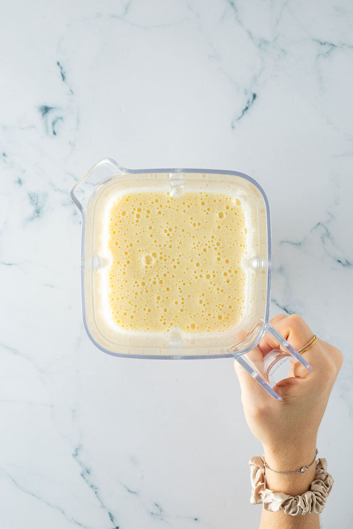 Hand hält einen Mixerbehälter mit pürierter Eiermischung für die meal prep Frühstückssandwiches.