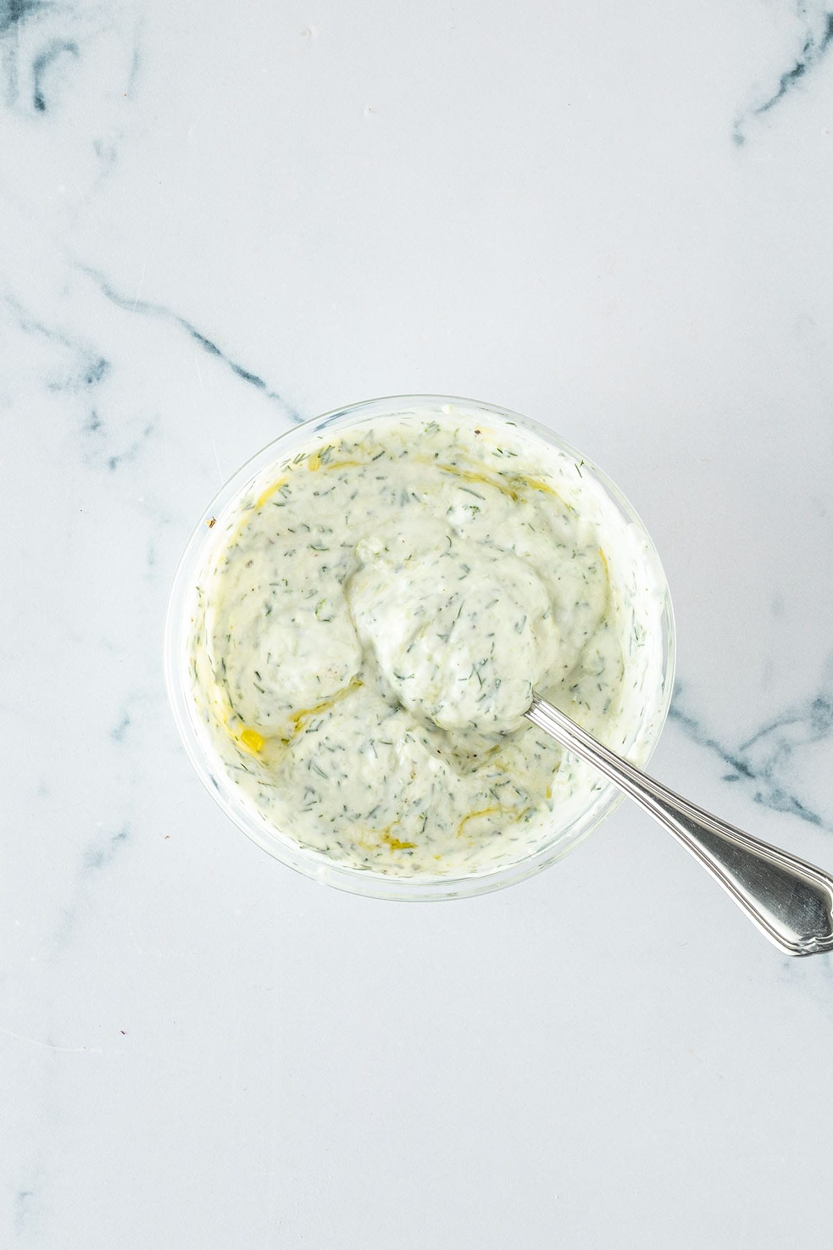 Cremiger Tzatziki mit geriebener Gurke und Dill in einer kleinen Glasschüssel.