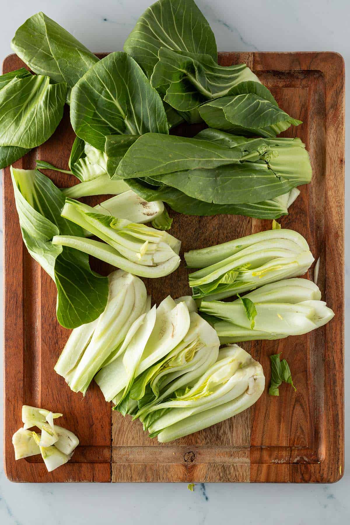 Pak Choi auf einem Holzbrett, halbiert und die unteren H&auml;lften geviertelt mit keilf&ouml;rmig herausgeschnittenen Strunk.
