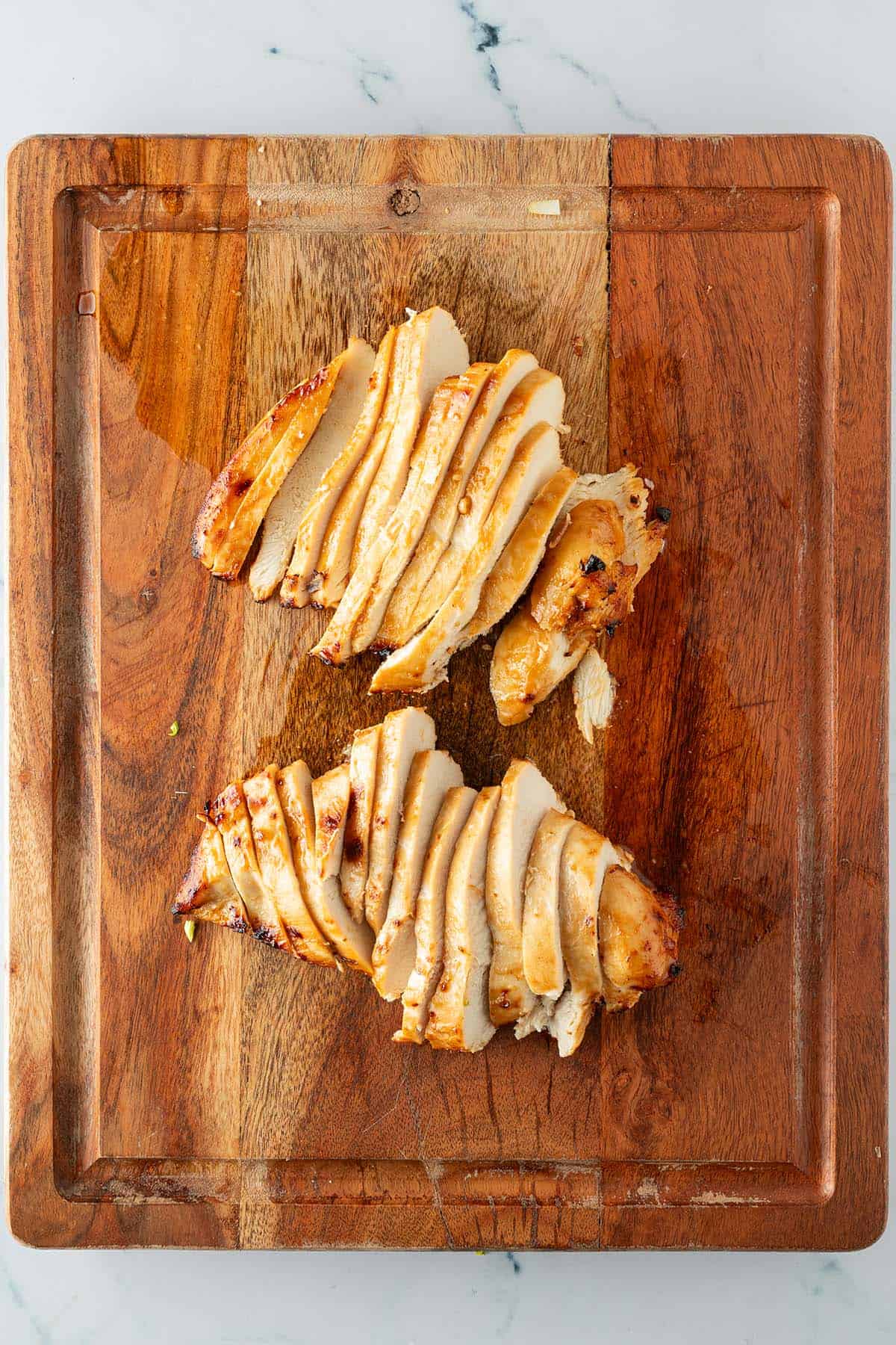 Gegarte H&auml;hnchenbrust auf einem Holzbrett in Scheiben geschnitten.