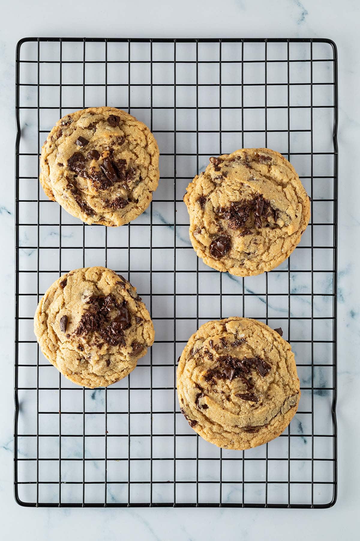 Vier frisch gebackene Chocolate Chip Cookies mit groben Schokostücken auf einem schwarzen Kuchengitter.