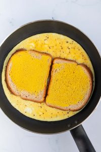 Omelett wird mit zwei Brotscheiben in einer Pfanne angebraten.