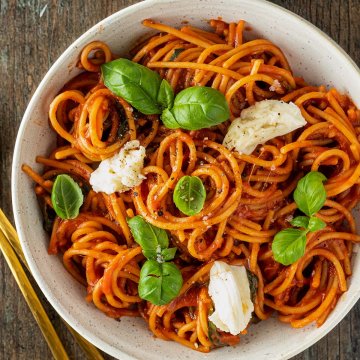 Teller Spaghetti in Tomatensauce mit frischem Mozzarella und Thunfisch auf einem Holzuntergrund.