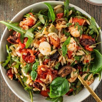 Vogelperspektive auf einen Teller mit einem Kritharaki-Nudelsalat mit Tomaten, Oliven, Mozzarella, Rucola und Tomaten.